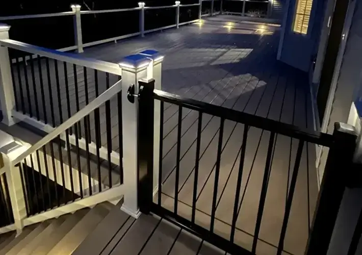 Spacious composite deck with integrated stair gate, black and white railing, and warm deck lighting creating an inviting evening atmosphere.