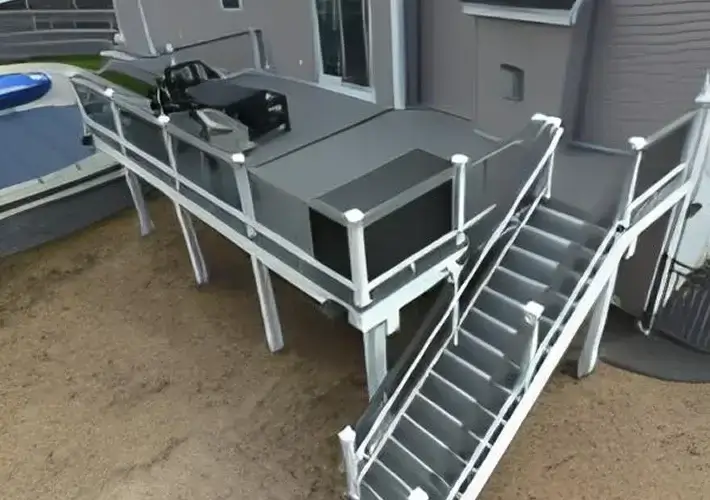 Modern gray composite deck with matching stairs, sleek white railings, and a built-in grilling station elevated on sturdy posts.